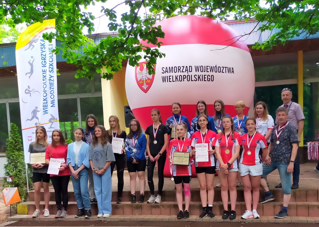 Zdjęcie przedstawia zwyciężczynie biegu na orientację w roku szkolnym 2020/2021 stojące na tle czerwono-białego balonu z logiem Samorządu Województwa Wielkopolskiego