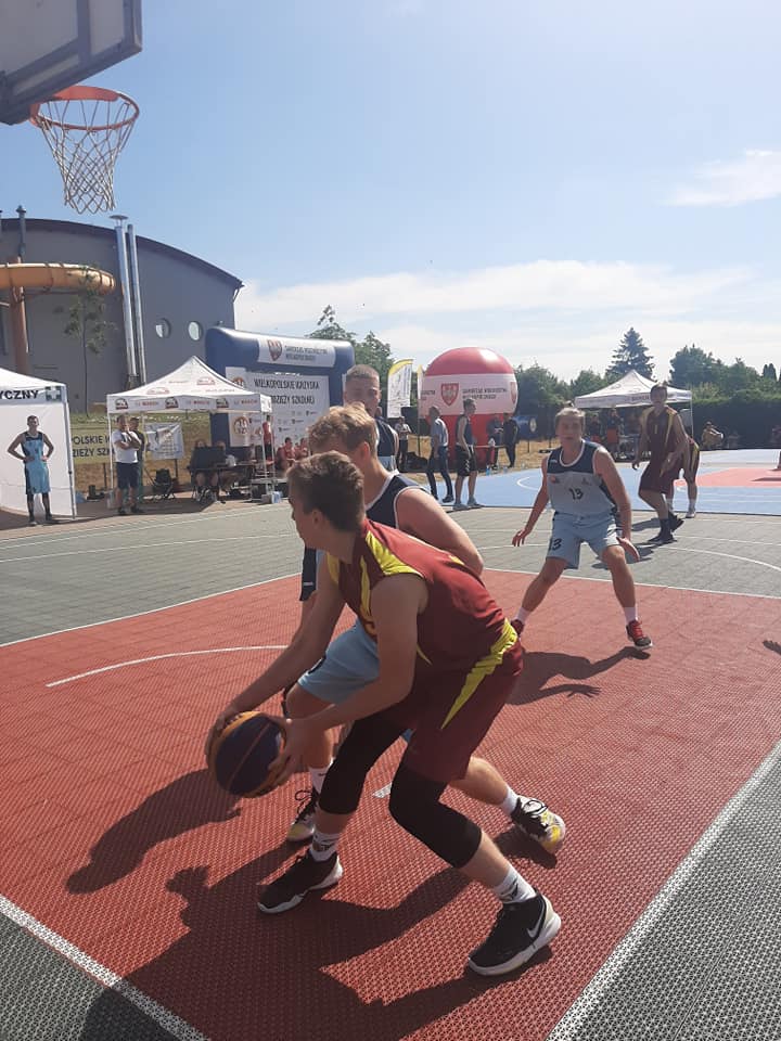 Zdjęcie przedstawia zawodników grających w koszykówkę 3x3, w tle widać pozostałych uczestników zawodów